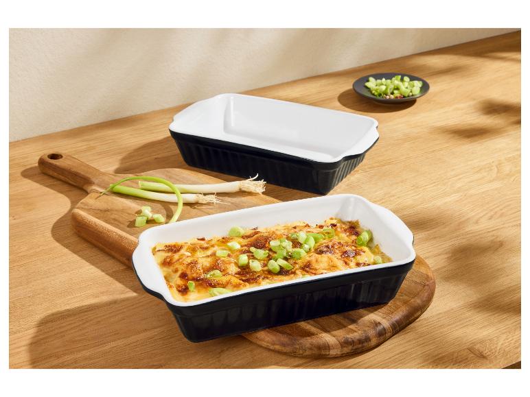 Twee rechthoekige ovenschalen, één gevuld met gratin en lente-uitjes, op een houten plank.