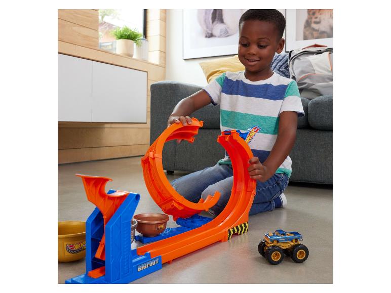 Een lachende jongen speelt met een Hot Wheels Monster Trucks baan en een auto.
