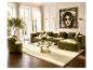 Elegante woonkamer met olijfgroene bank, fauteuil, glazen salontafel en licht tapijt.