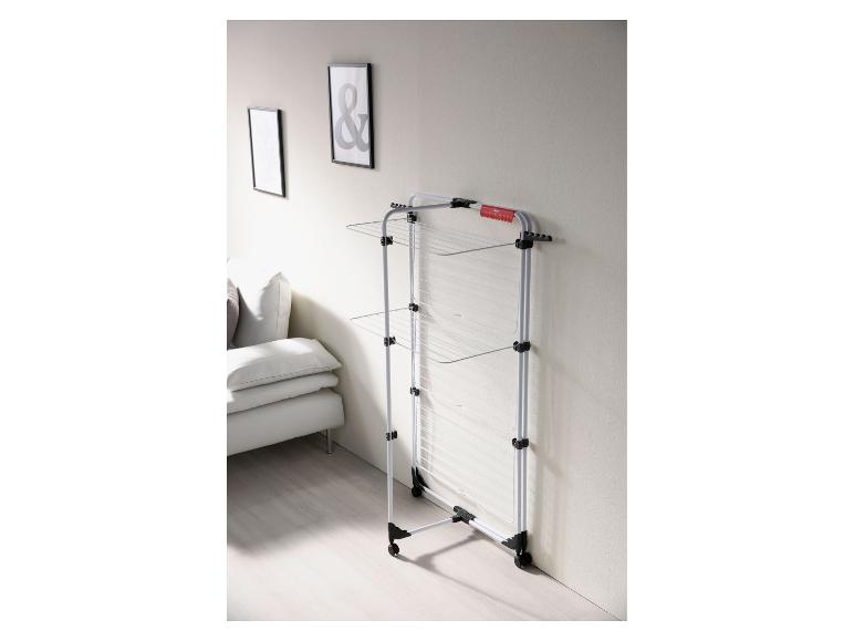 Wit wasrek met drie niveaus, naast een lichtgrijze bank en ingelijste kunst.