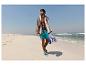 Man in zwembroek en met handdoek loopt op het strand.