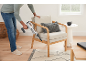 Man reinigt een lichte fauteuil met een handstofzuiger in een lichte woonkamer.