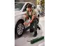 Een man in groene overall en beige T-shirt draait een wielmoer vast aan een witte auto.