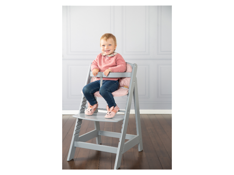 Een meisje zit op een grijze Stokke Tripp Trapp kinderstoel.