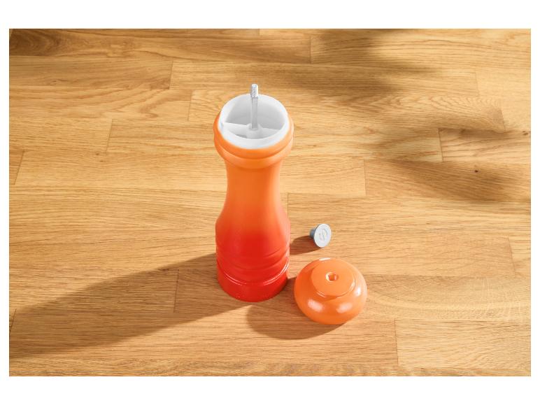 Oranje pepermolen met losse dop op een houten ondergrond.