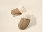Paar beige suède pantoffels met crèmekleurige imitatiebont voering, één iets achter de ander.