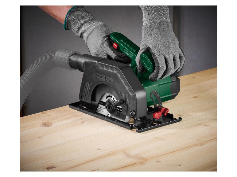 Een persoon met handschoenen gebruikt een Parkside mini cirkelzaag op een houten oppervlak.