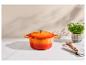Oranje gietijzeren pan met deksel, ovenwant, houten lepel en peterselie in pot op een marmeren oppervlak.
