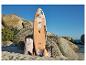 Stand-up paddleboard met bloemendesign, rugzak, peddel en pomp op een rotsachtig strand.