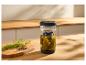 Glazen pot met ingelegde augurken en knoflook, dille en peperkorrels op een houten plank.