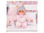 Babypop in roze pyjama met speen en fles, zittend in een wit ledikant.
