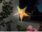 Verlichte decoratieve ster hangt buiten met een groene tuinafbeelding.
