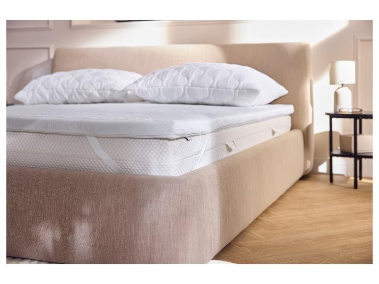 Slaapkamer met een bed met een matrasoplegger, matras en twee kussens.