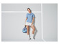 Een vrouw in een blauwe polo en witte rok houdt een padelracket vast.