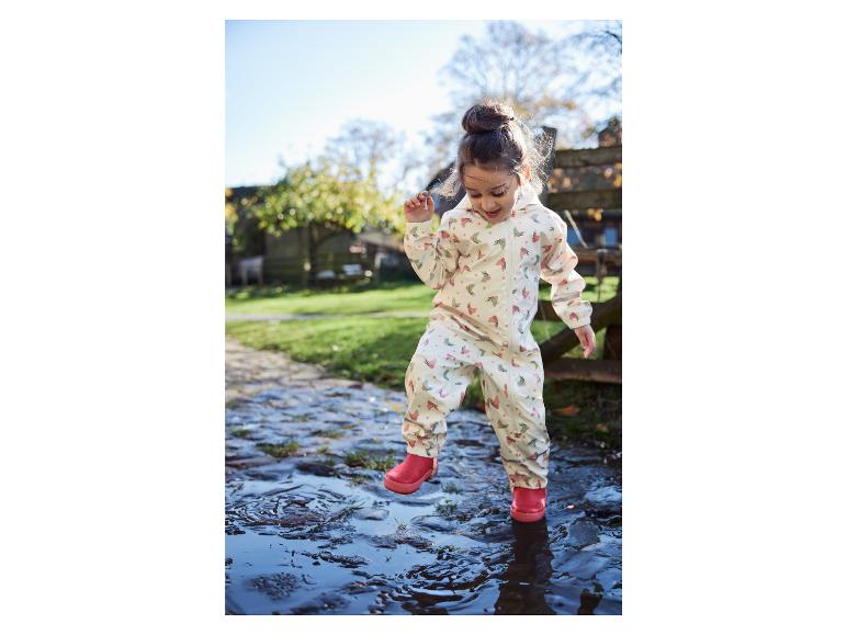 Een kind in een regenpak met vlinderprint springt in een plas.