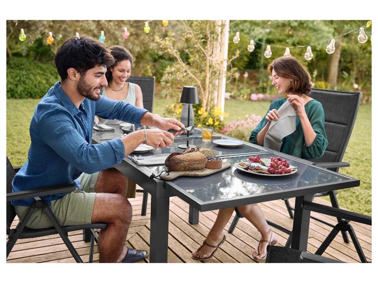 Drie mensen genieten van een buitenmaaltijd op een terras met een tuintafel en stoelen.