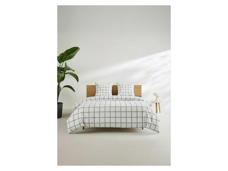 Bed met geruit beddengoed, houten hoofdbord, plant en nachtkastje met lamp.