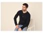 Man in een zwart Henley-shirt met lange mouwen en jeans, zittend op een stoel.
