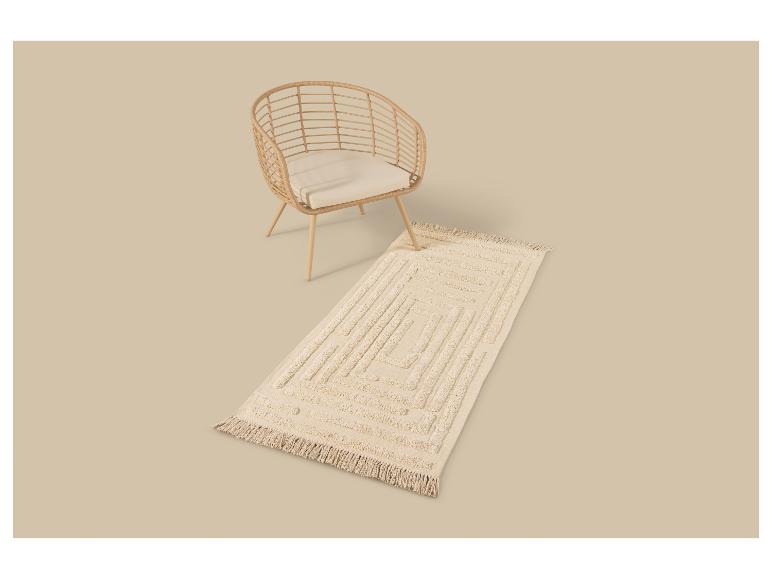 Rotan fauteuil met crèmekleurig kussen en rechthoekig vloerkleed met geometrisch patroon.