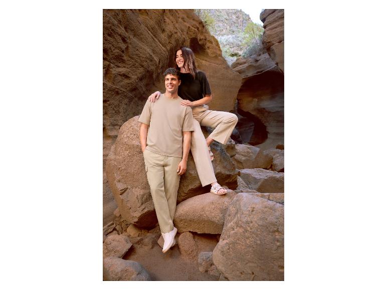 Man en vrouw in casual beige en zwarte kleding, staand tussen rotsen.