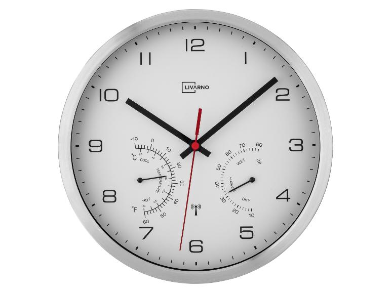 Een witte wandklok met thermometer en hygrometer, met een zilveren frame.