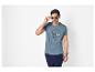 Man in blauw T-shirt met maritieme print, donkerblauwe broek en zonnebril.