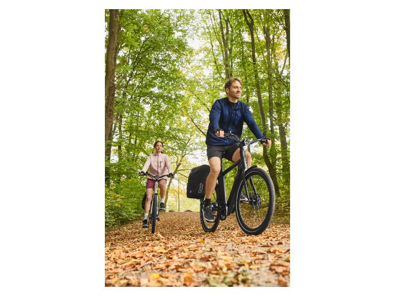 Twee mensen fietsen op een bospad bedekt met herfstbladeren.