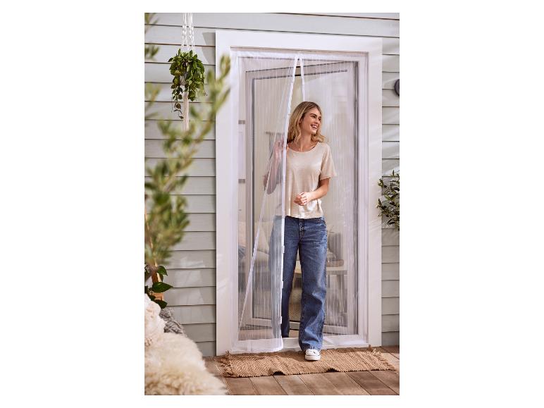 Een vrouw staat in een deuropening met een magnetisch vliegengaas.