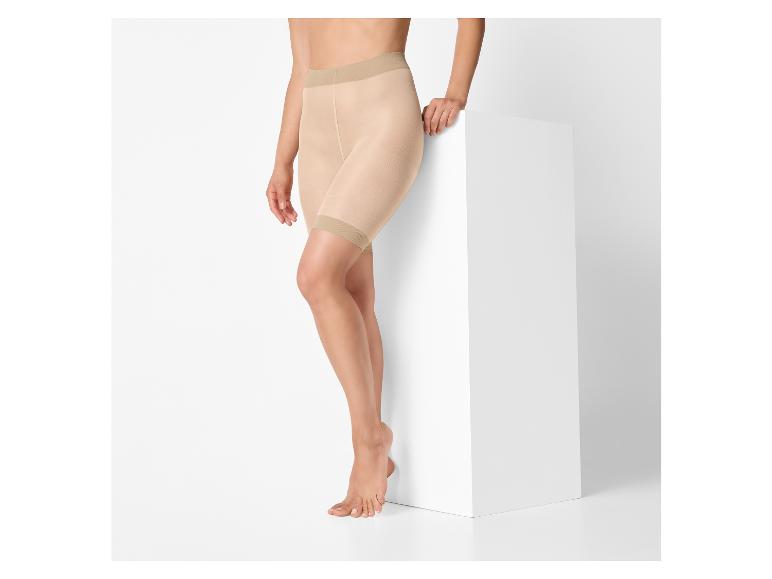 Vrouw draagt huidkleurige corrigerende shorts, staand naast een witte kubus.