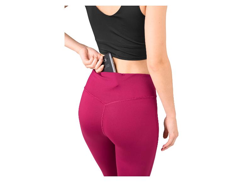 Vrouw in zwarte top en roze legging stopt telefoon in zak.