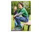 Man in groen T-shirt en spijkeroveralls, met groene sneakers, zittend op een houten bankje.