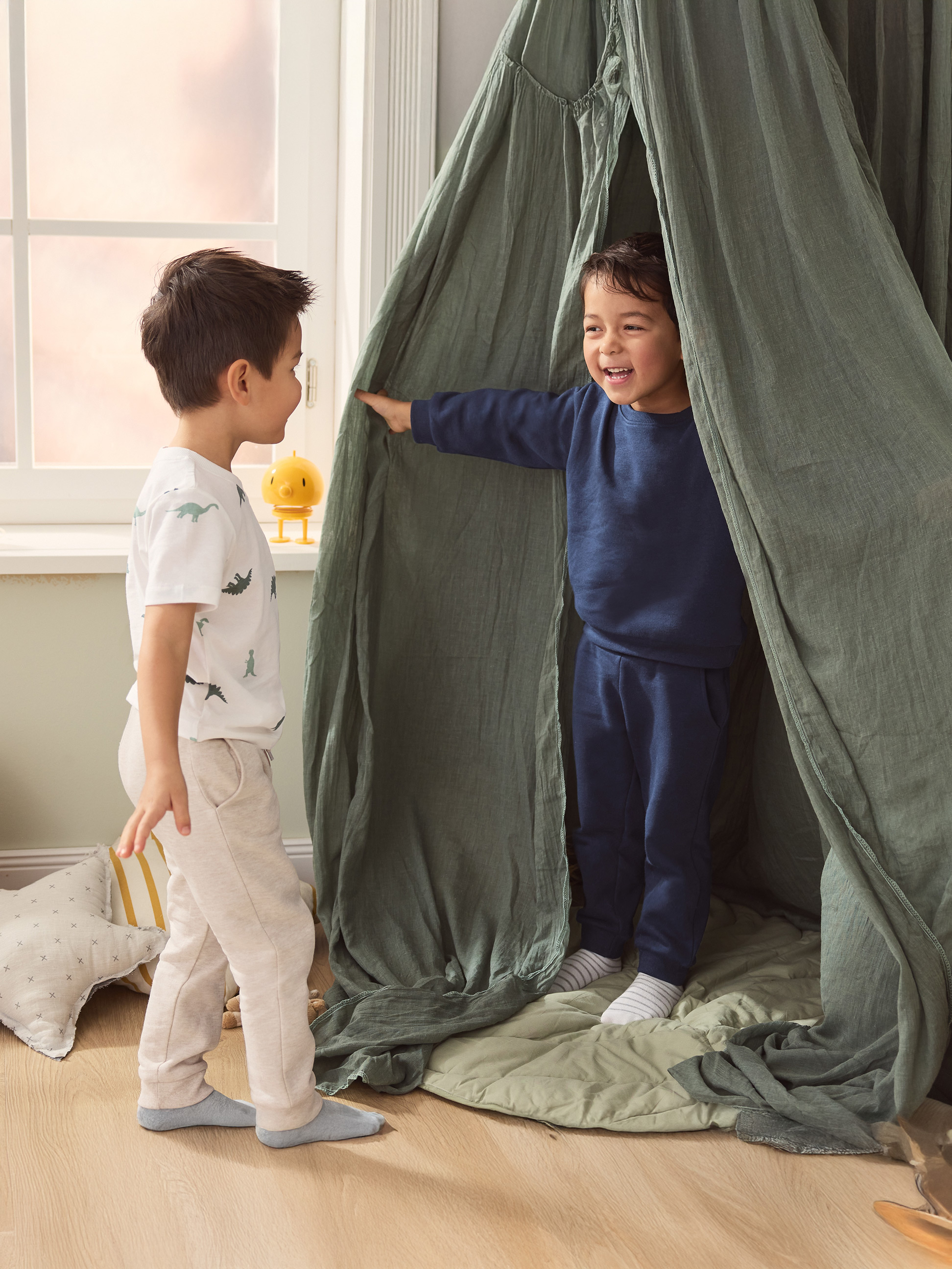 Twee jongens spelen in een groene speeltent, één draagt een dinosaurus T-shirt.
