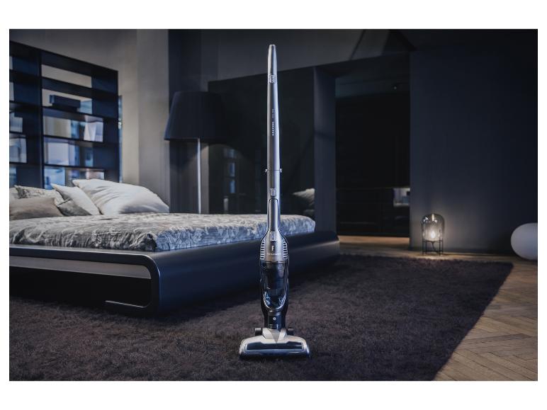 Een Grundig steelstofzuiger in een moderne slaapkamer met een bed en vloerkleed.