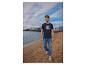 Man in marineblauw T-shirt en jeans op een zandstrand.