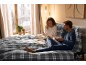Een stel in gezellige pyjama's ontbijt in bed met grijs geruit beddengoed.