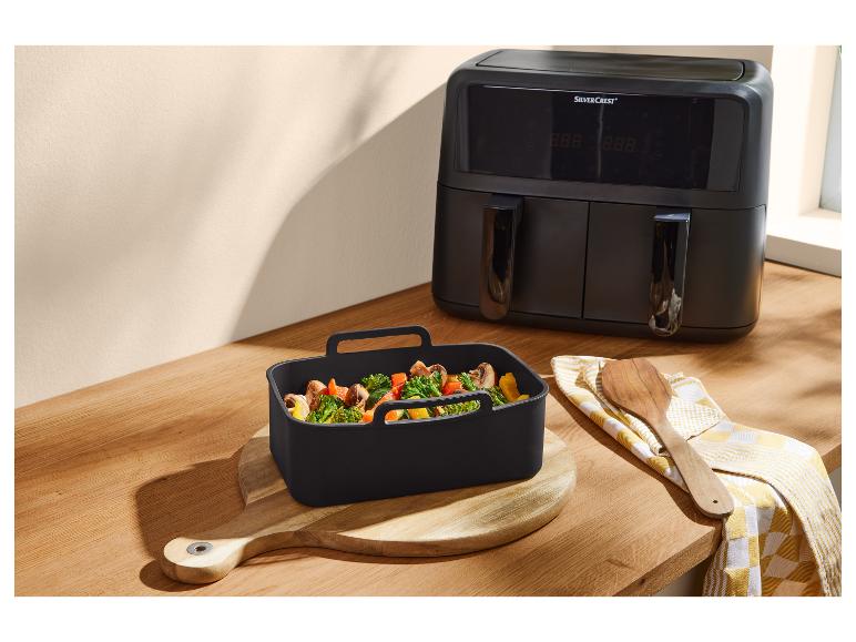 Zwarte dubbele airfryer en siliconen schaal met groenten op een houten aanrecht.