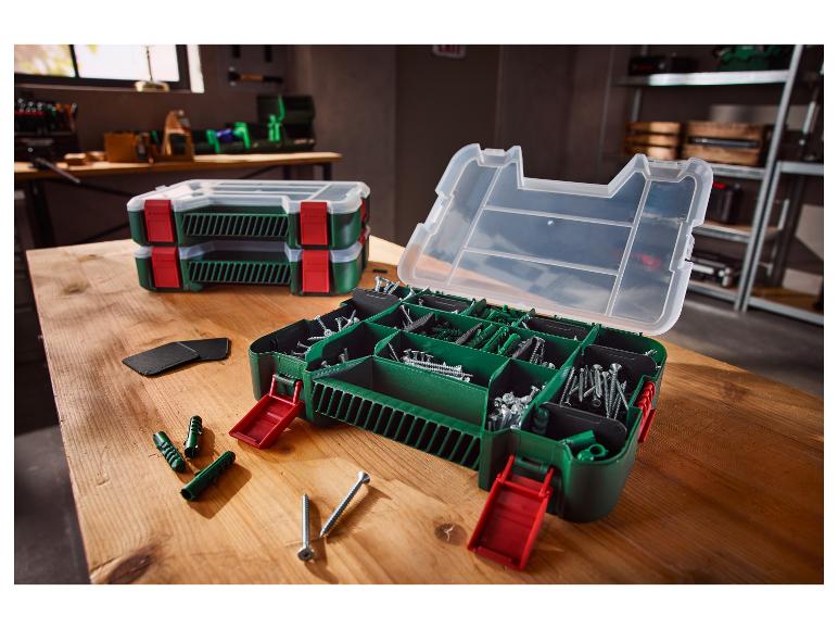 Open gereedschapskist met schroeven en pluggen op een houten tafel, met twee gesloten kisten op de achtergrond.