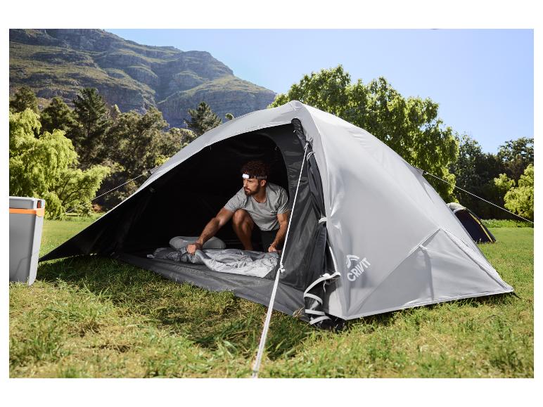 Man in grijze tent, bereidt slaapzak voor in berglandschap.