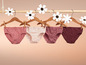 Vier paar roze onderbroeken hangen aan houten hangers met bloemenversiering.
