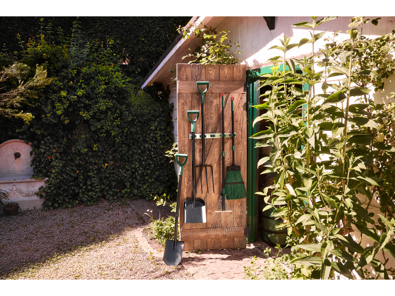 Tuin gereedschap hangend aan een houten deur, met een schop en hark op de voorgrond.