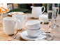 Wit porseleinen servies: mokken, kopjes, schotels, melkkan en suikerpot op houten tafel met champagneglazen en sterkoekjes.