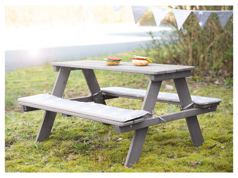 Grijze kinderpicknicktafel met kussens en speelgoedeten op het gras.