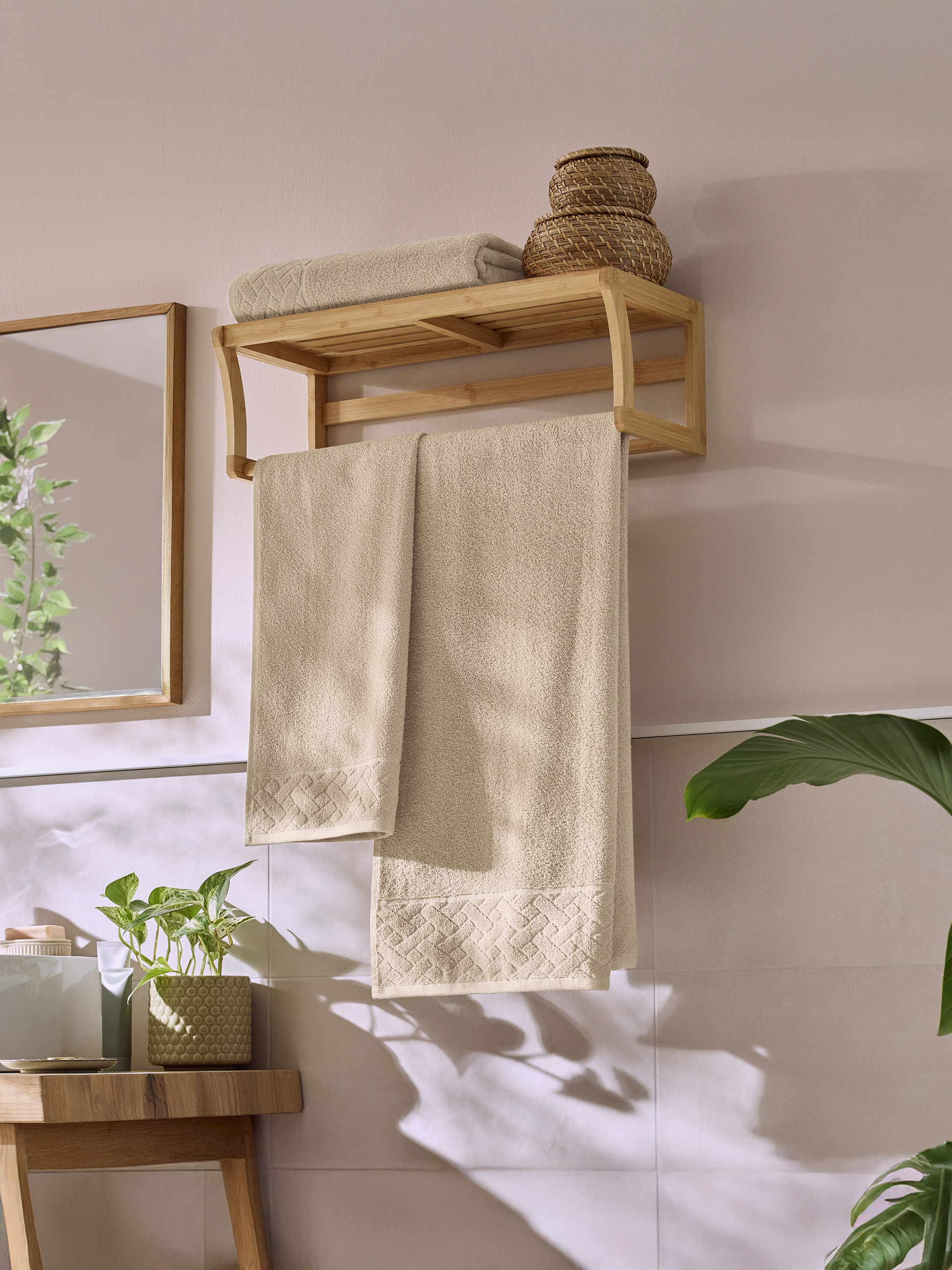 Badkamer met een houten handdoekenrek, beige handdoeken en groene planten.