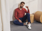Man met rood shirt en blauwe jeans draagt witte sneakers.