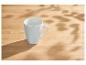 Witte mok op een houten tafel met bladerschaduwen.