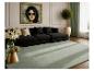 Moderne woonkamer met zwarte bank, lichtgroen vloerkleed, gouden salontafel en wanddecoratie.