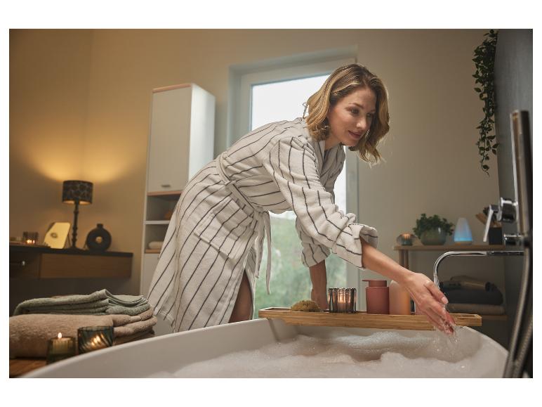 Een vrouw in een badjas bereidt een schuimbad voor.