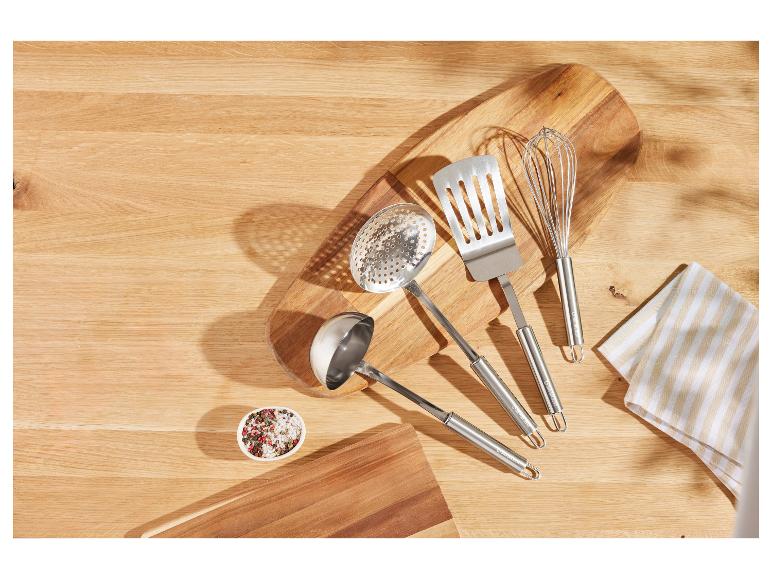 Roestvrijstalen keukengerei, waaronder een spatel, pollepel en garde, op een houten snijplank.