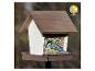 Een koolmees in een houten vogelvoederhuisje gevuld met zaden, met het 'ganzjährig füttern' logo.