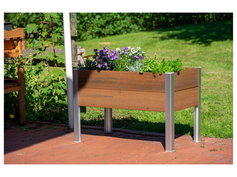 Een houten plantenbak met bloemen en kruiden op een terras.